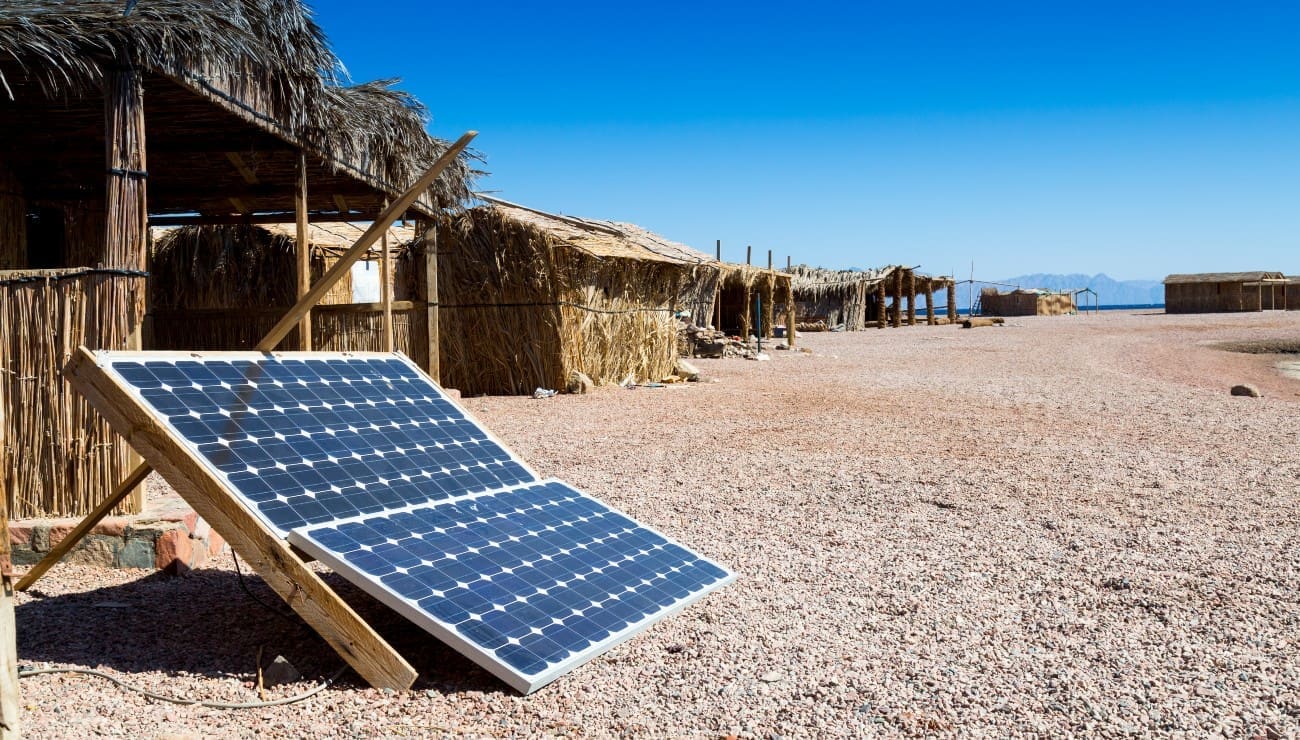 Panneau solaire avec des huttes au toit de chaume en arrière-plan - RA-ESG